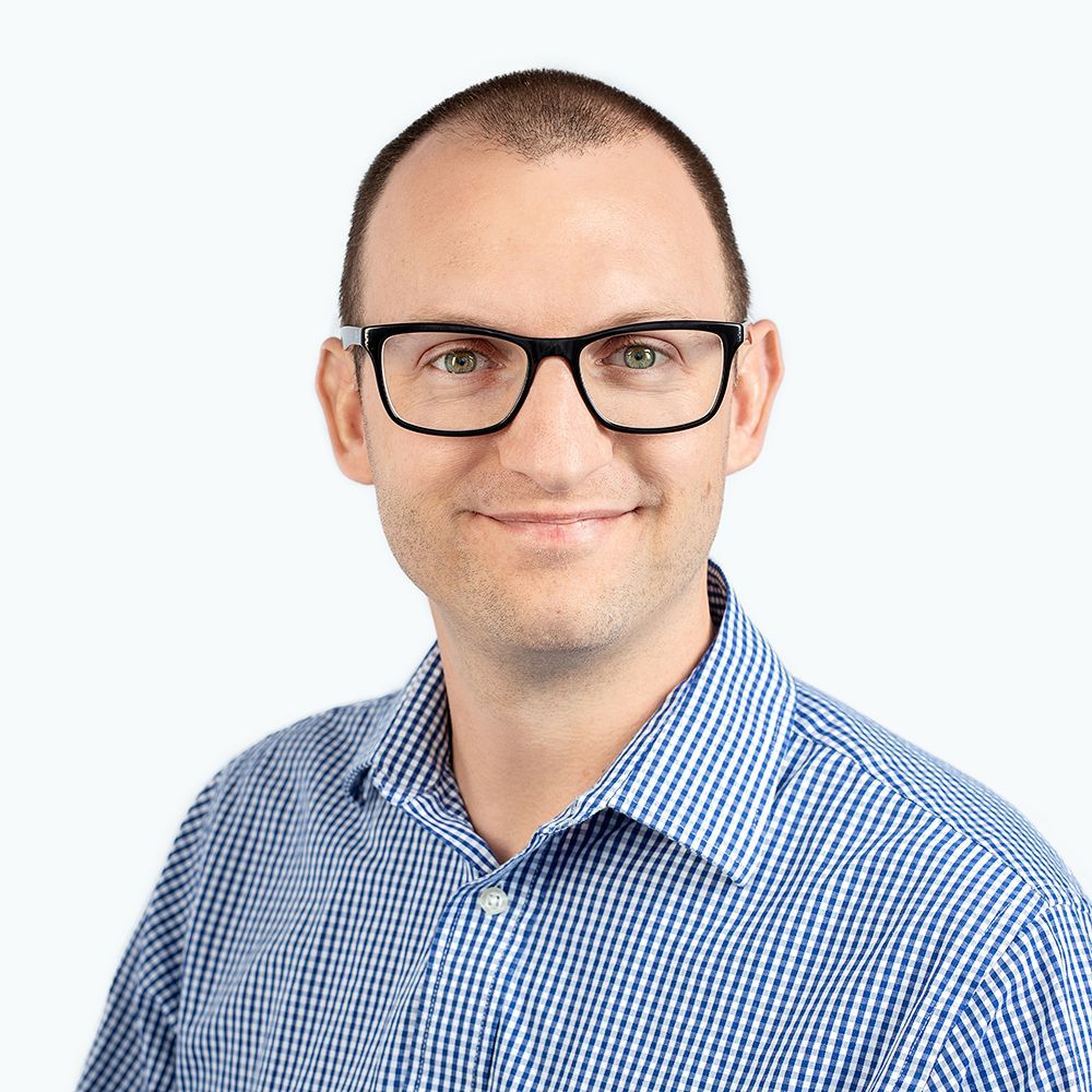 Agent Justin wearing glasses and a blue plaid shirt is smiling for the camera.
