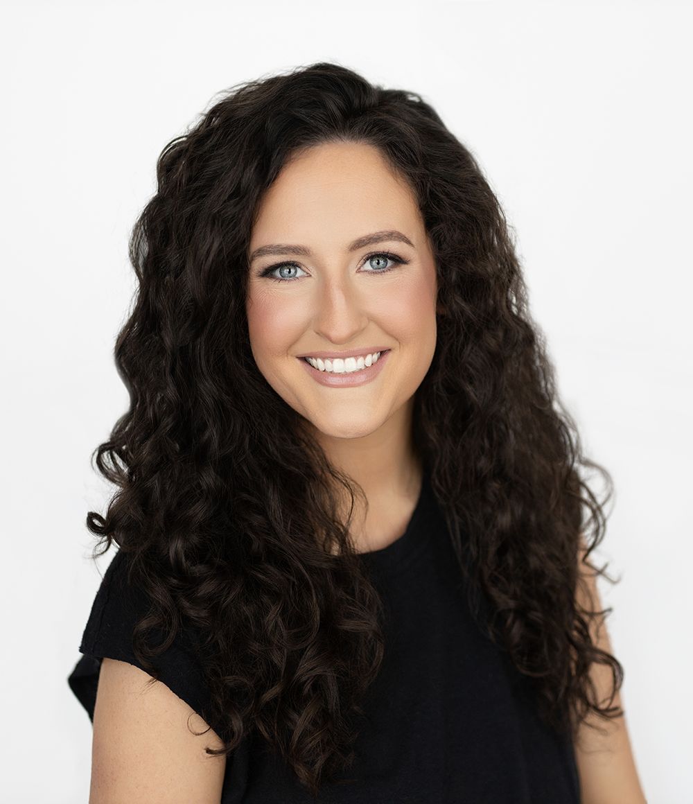 Agent Casey with curly hair is wearing a white jacket and smiling.