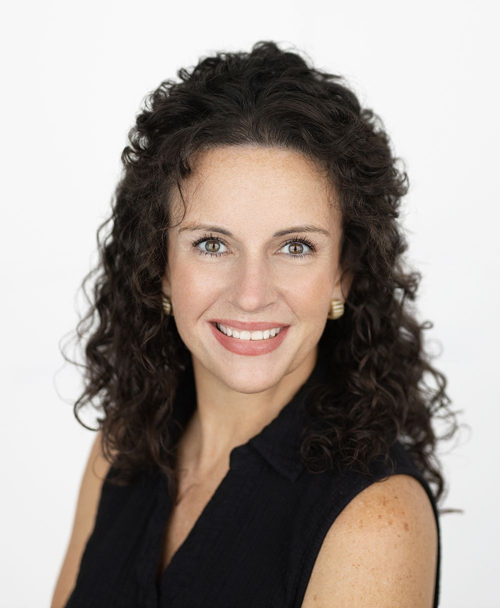 Agency owner Jennifer with curly hair is wearing a green shirt and smiling.