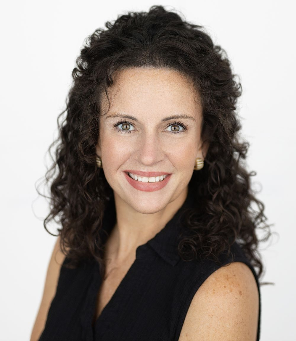 Agency owner Jennifer with curly hair is wearing a green shirt and smiling.
