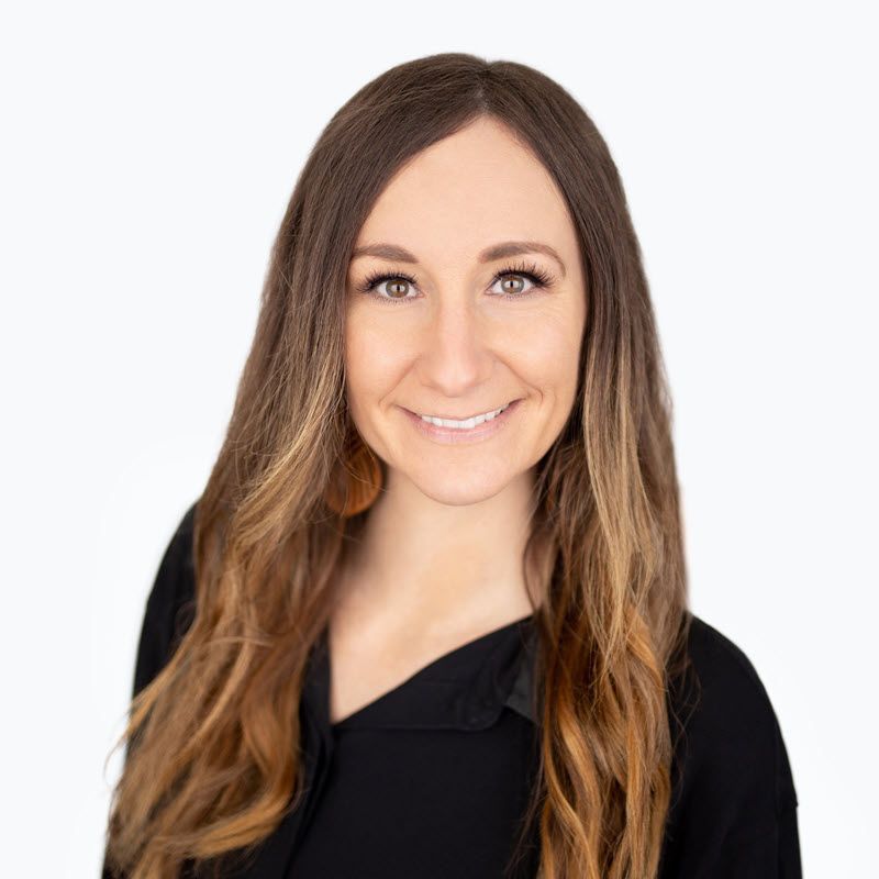 Office Manager Kelly with long brown hair is wearing a black shirt and smiling.