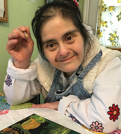 Family of three smiles on grass: woman, teen with Down syndrome, man.
