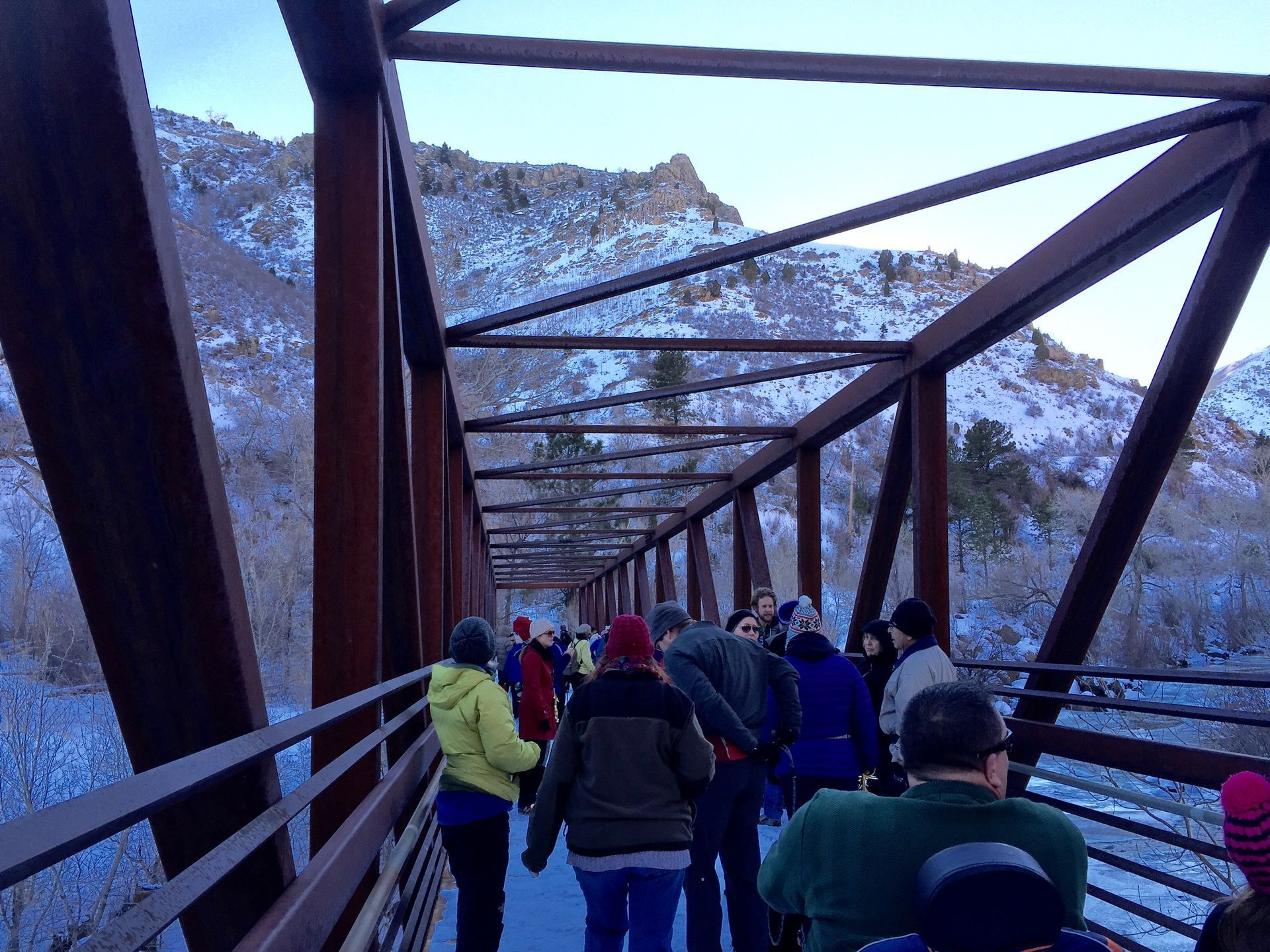 people out for a stroll on a bridge with snow covered mountains behind