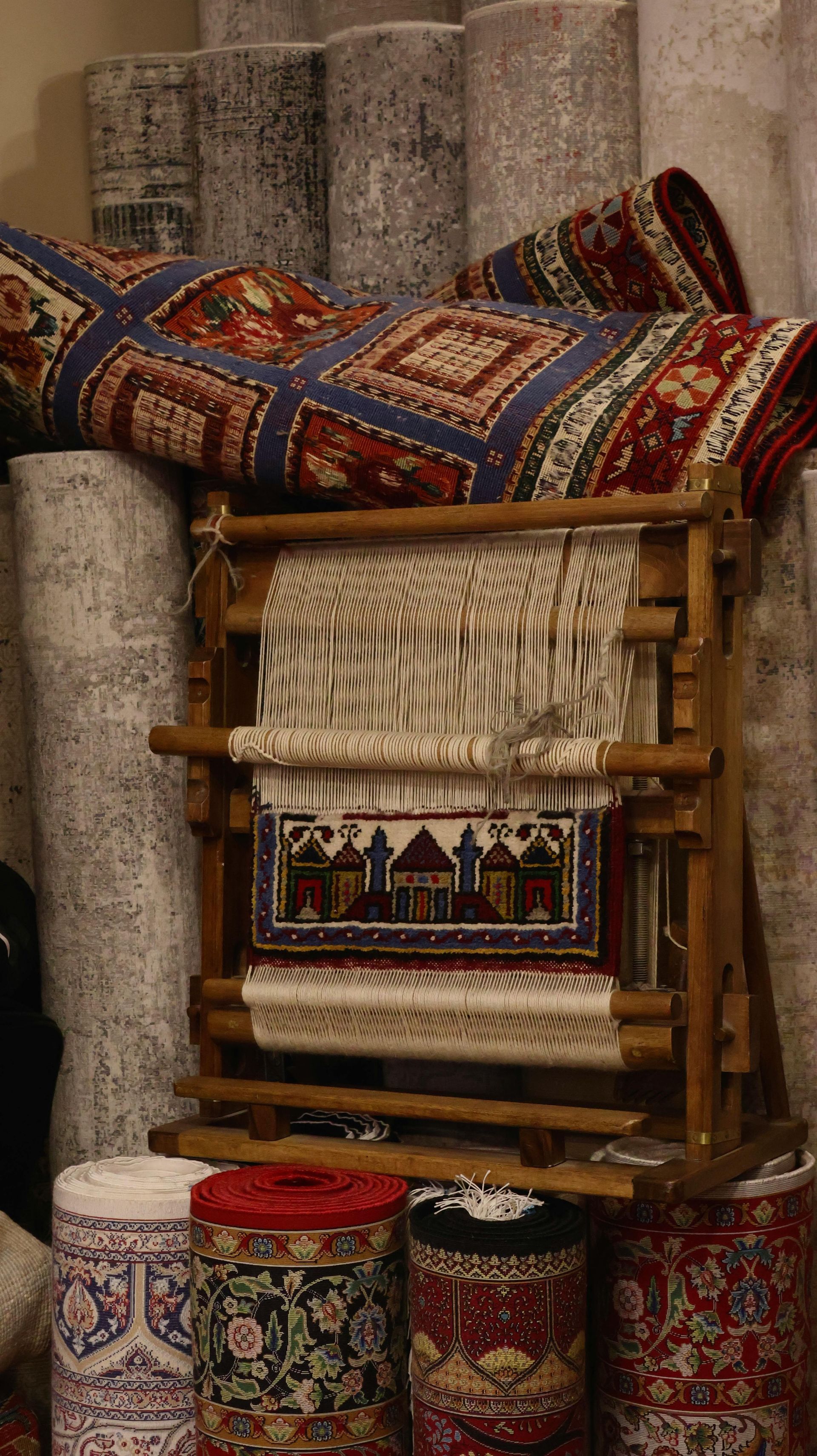 A rug on a loom shows a pattern of buildings partially completed