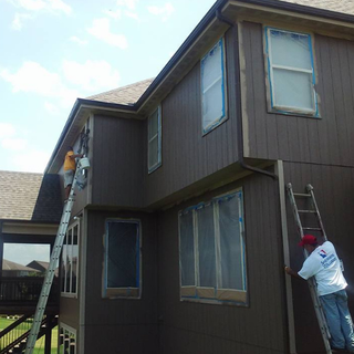 A man on a ladder paints the side of a house