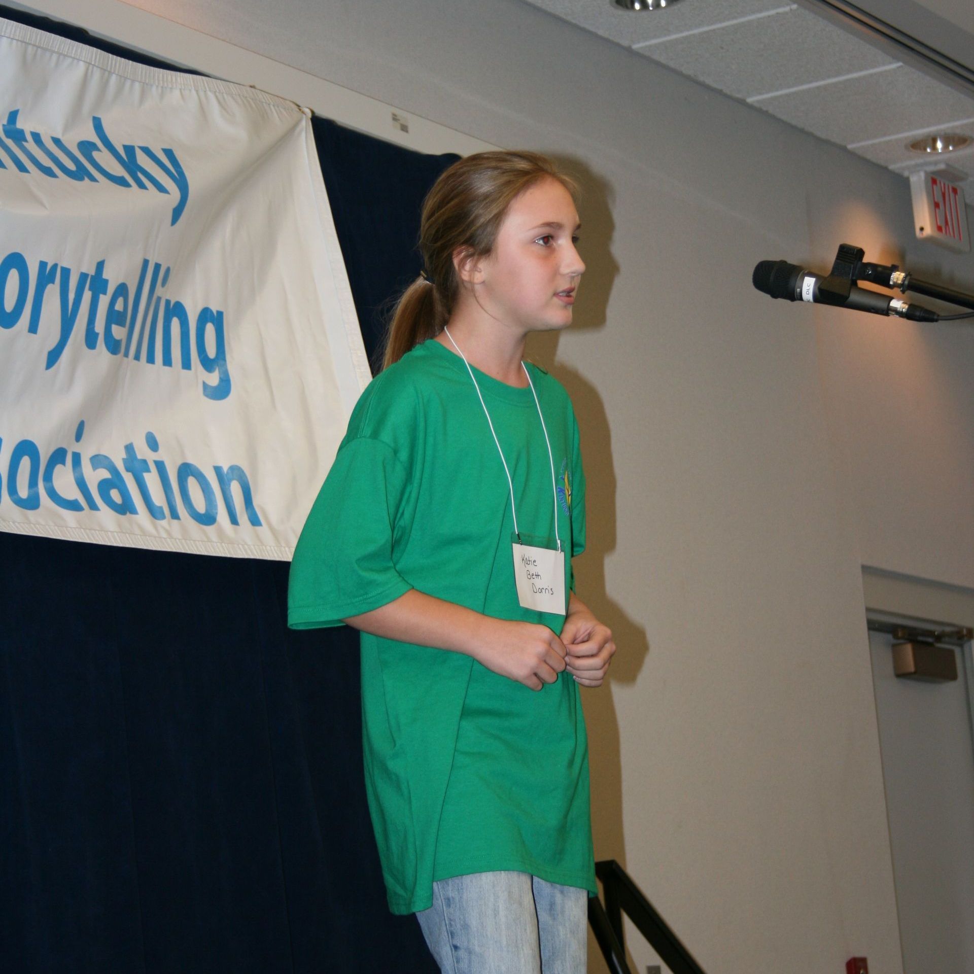 Young girl with a name badge standing in front of a microphone.