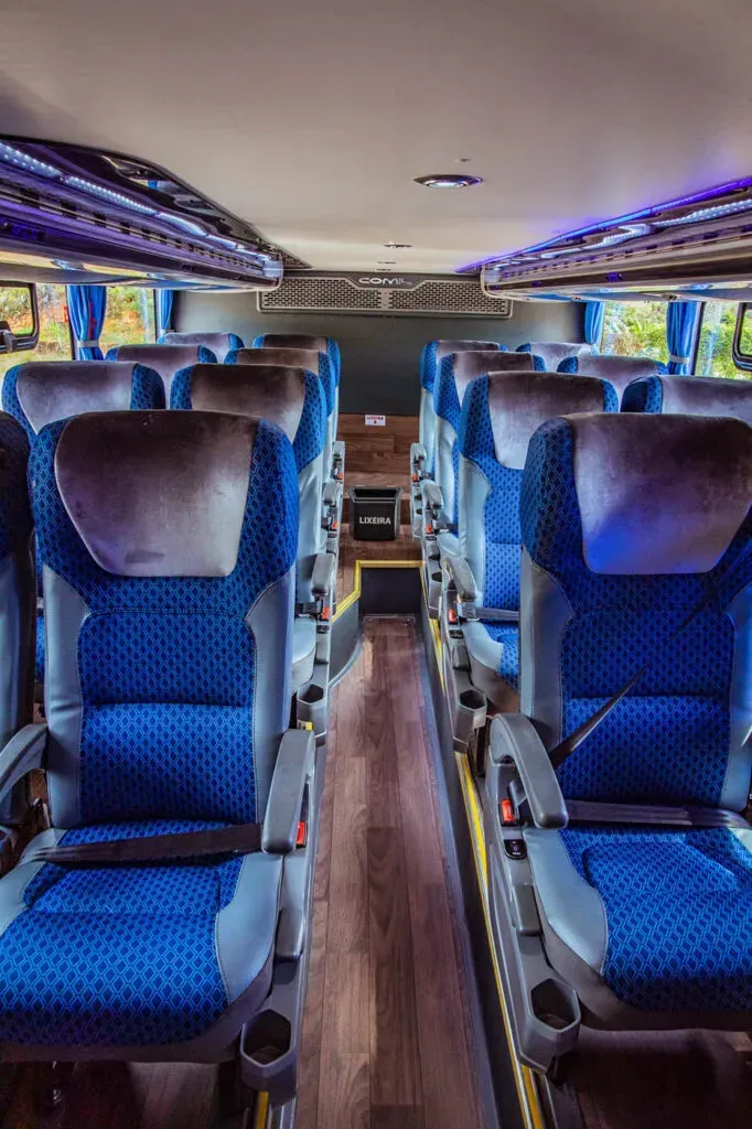 O interior de um ônibus com assentos azuis e piso de madeira.