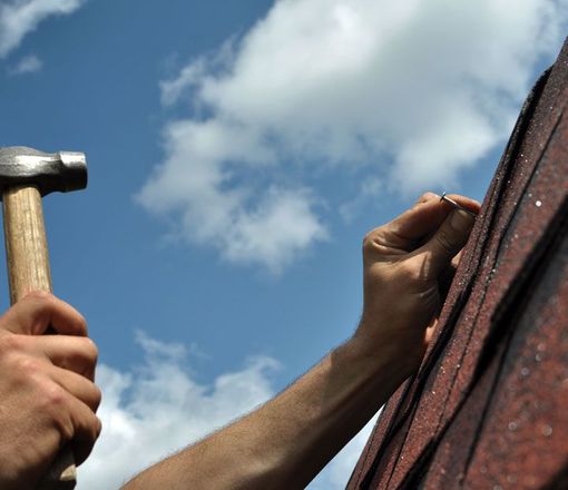 Hand with a hammer to drive a nail, roof repairs 
