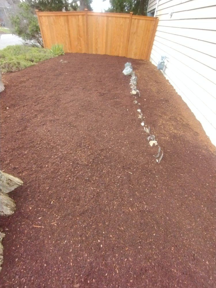 Brown mulch bed next to a white house, with a wooden fence in the background.