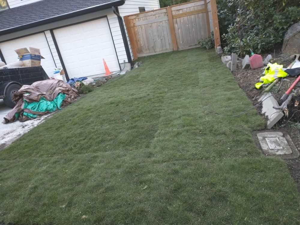 Freshly laid sod in a narrow yard, next to a garage and wooden fence; tools and materials nearby.