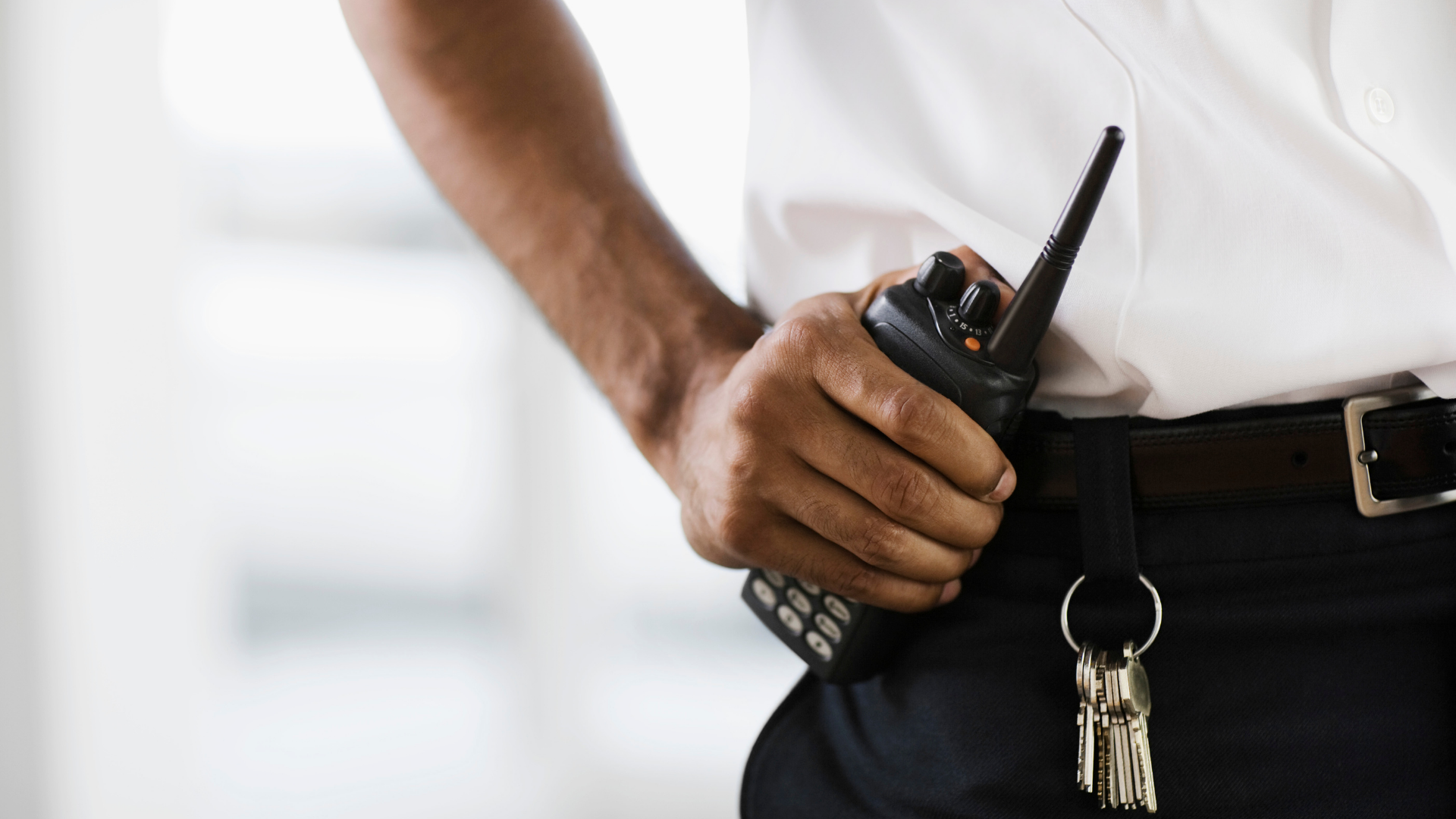 A security guard is holding a walkie talkie in his hand.