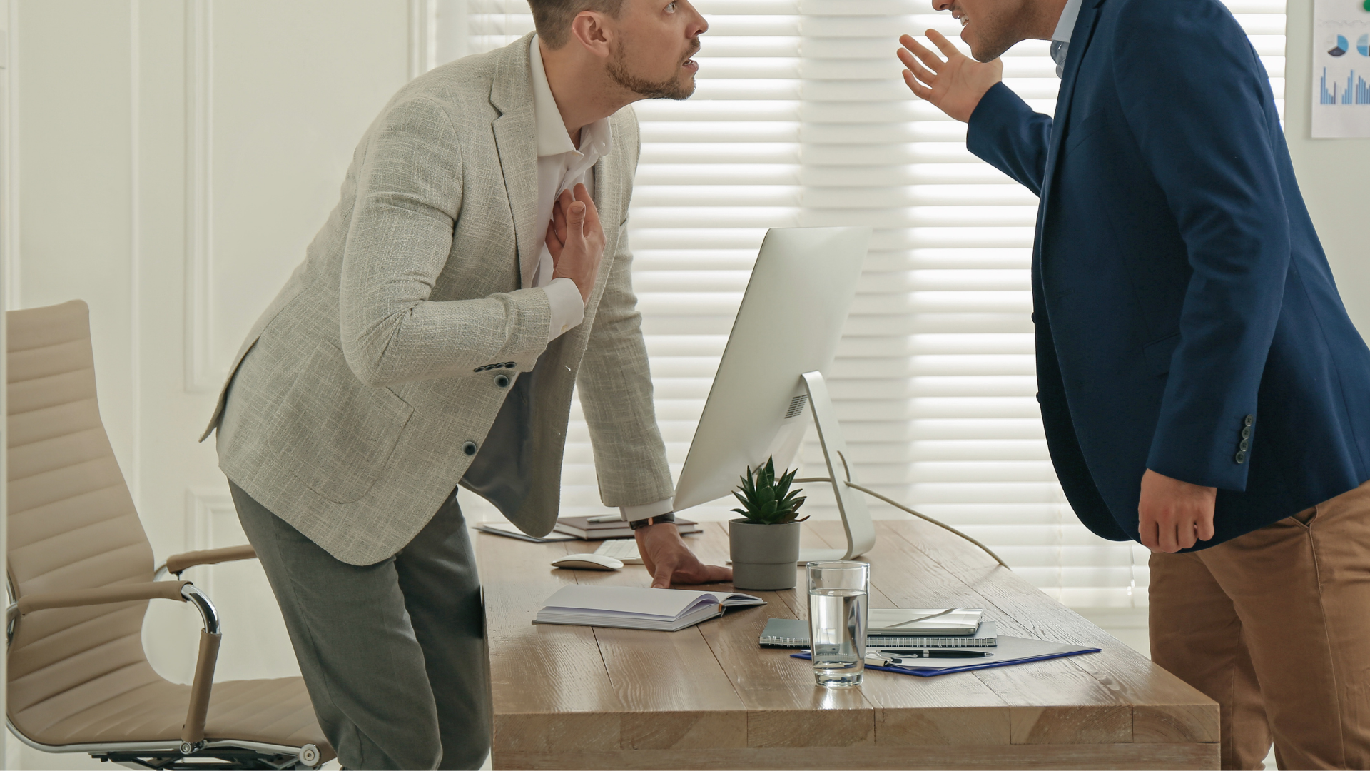 Two men are having an argument in front of a computer in an office.