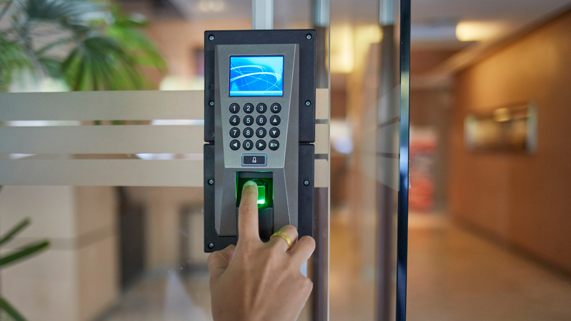 A person is using a fingerprint scanner on a glass door.