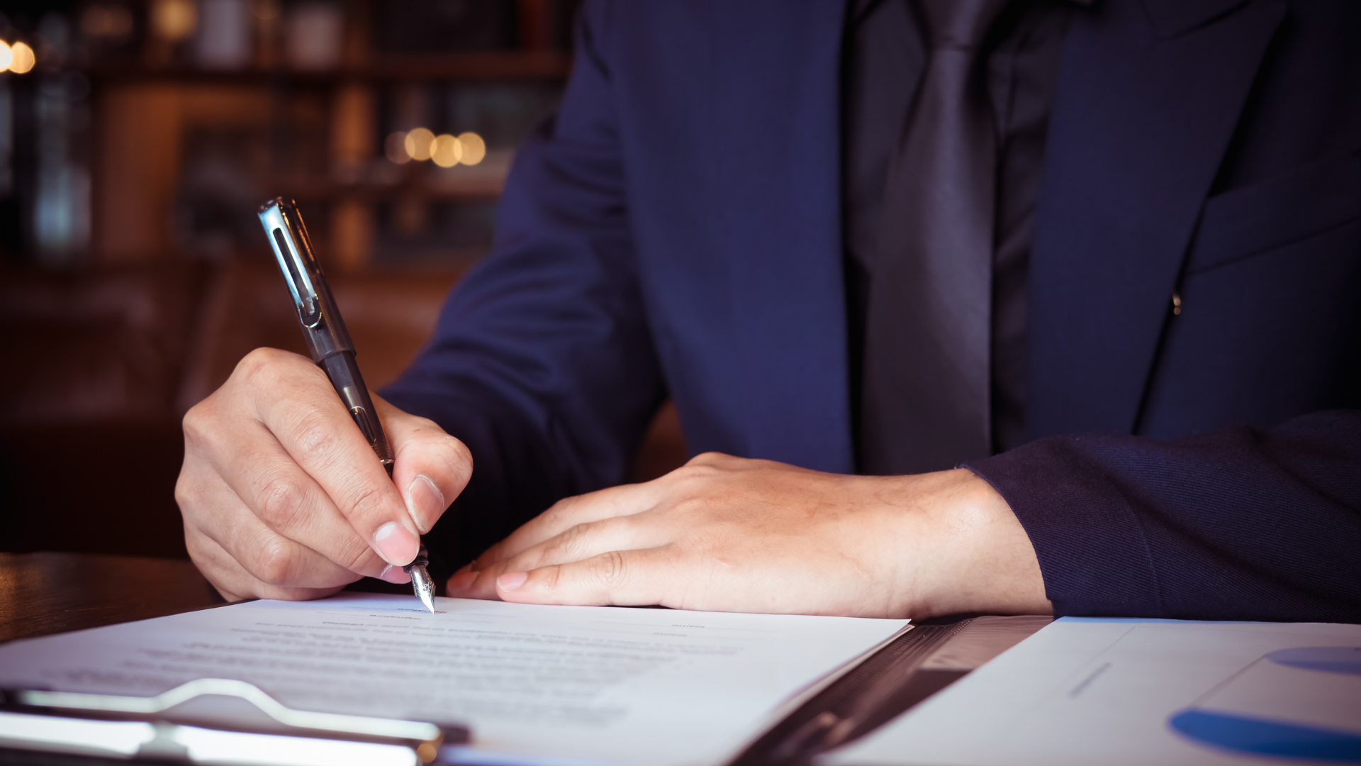 A man in a suit and tie is signing a document with a pen.