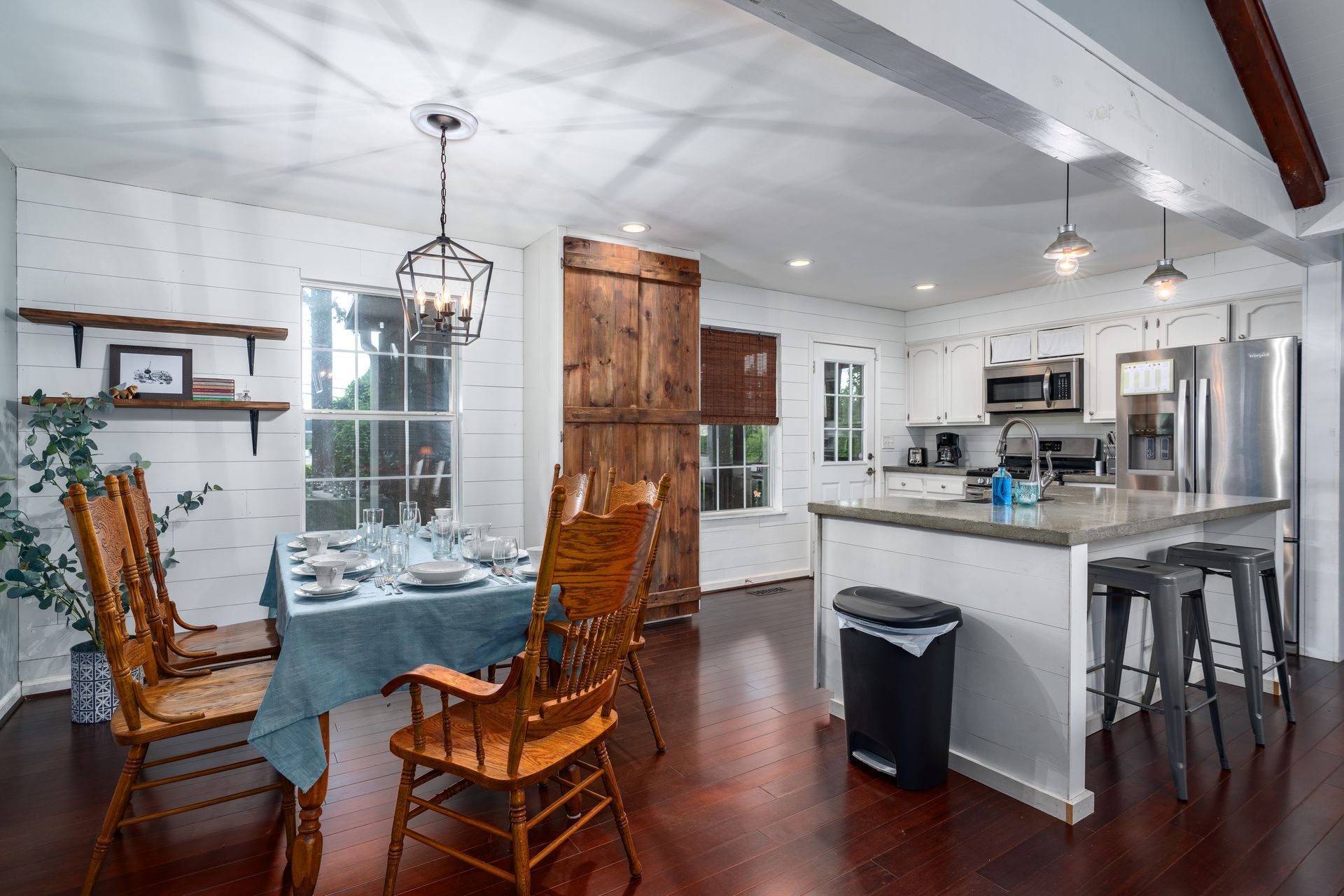 A dining room with a table and chairs and a kitchen with stainless steel appliances.