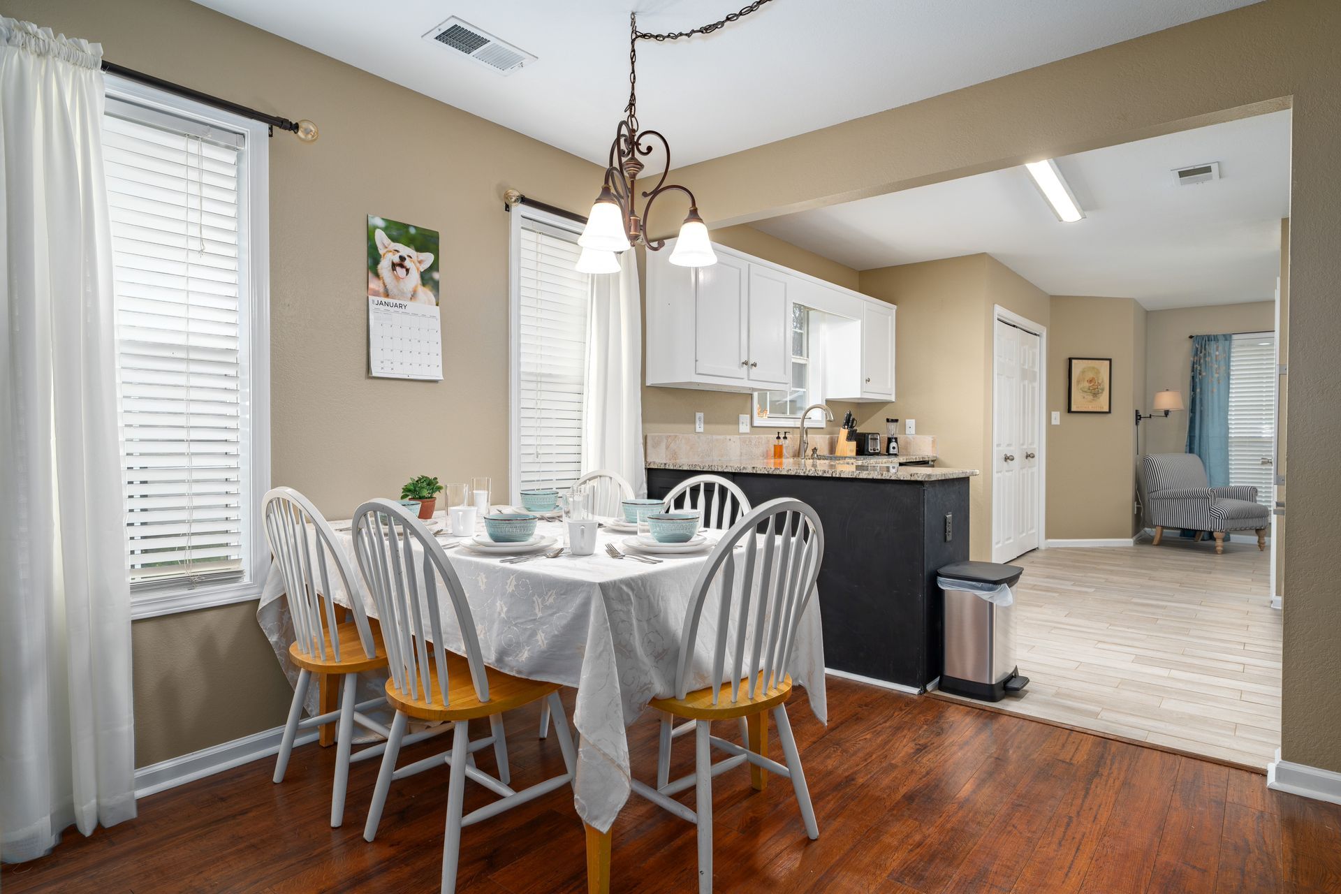 A dining room with a table and chairs and a kitchen in the background.