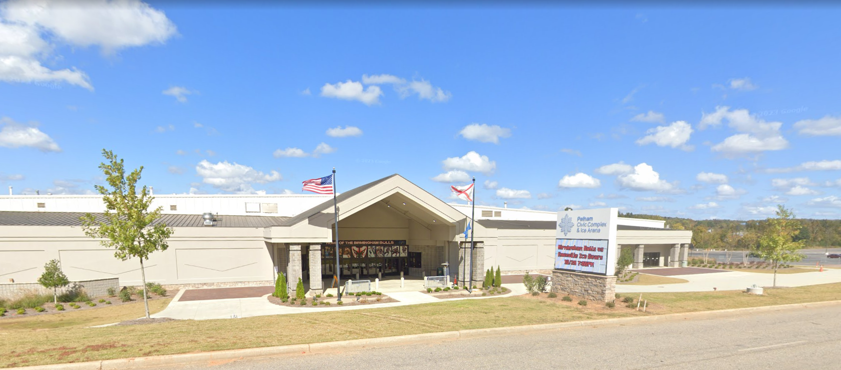 A light-colored building with a peaked entrance under a bright blue sky. A sign is to the right.