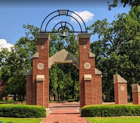 Red brick bell tower at the end of a brick path, trees, and blue sky.