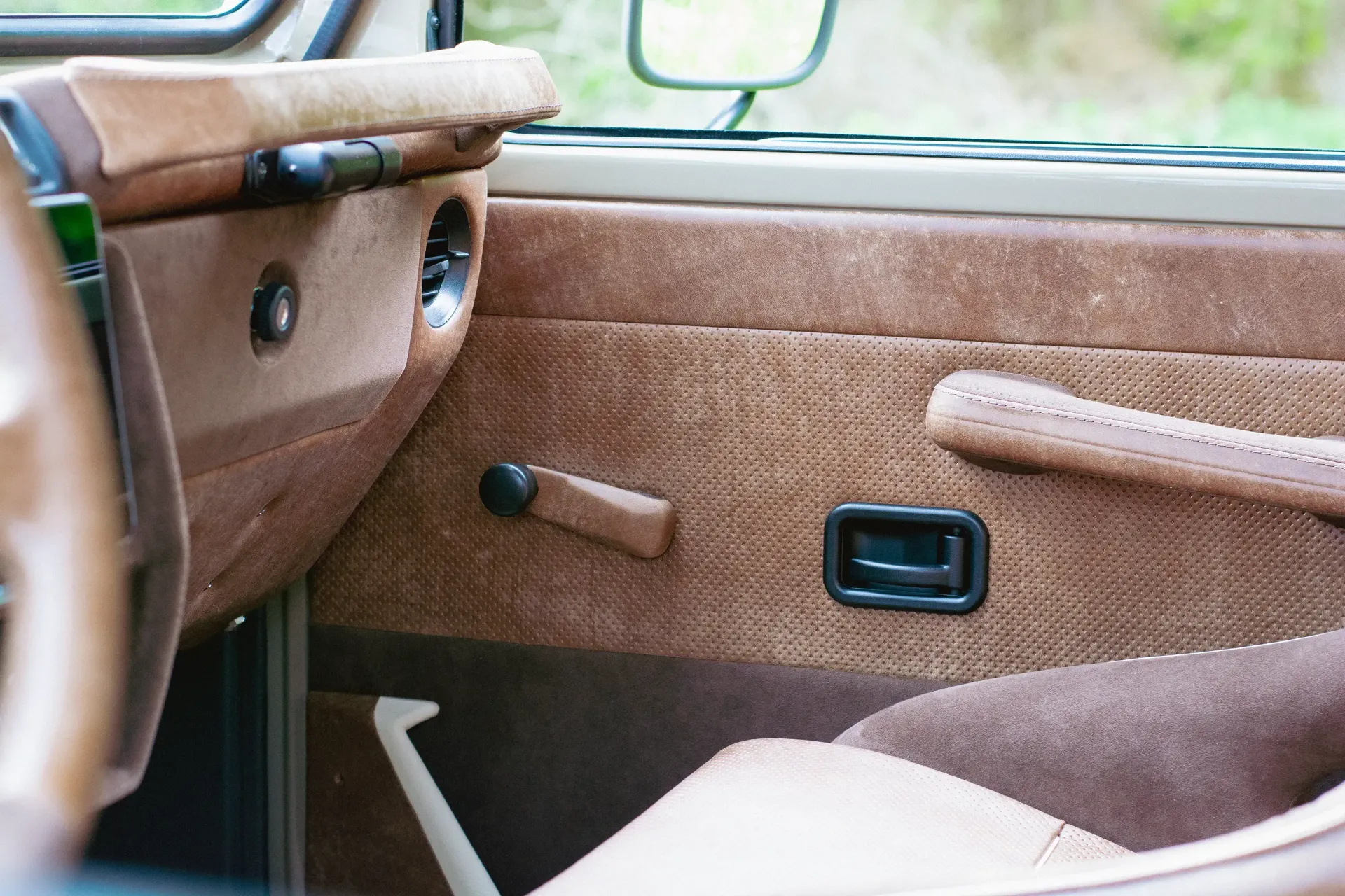 A close up of a car door with a leather steering wheel