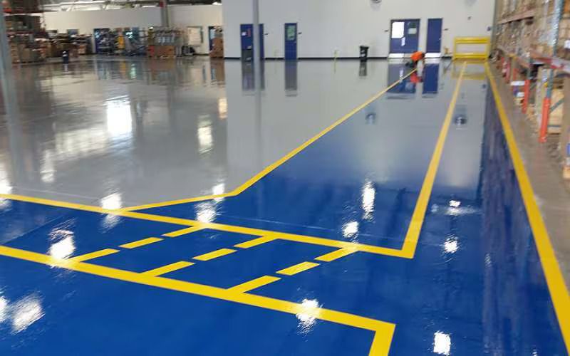 Blue and gray industrial floor with yellow markings in a warehouse setting.