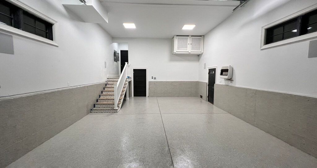 Empty, freshly painted garage with a speckled epoxy floor and a staircase leading upstairs.