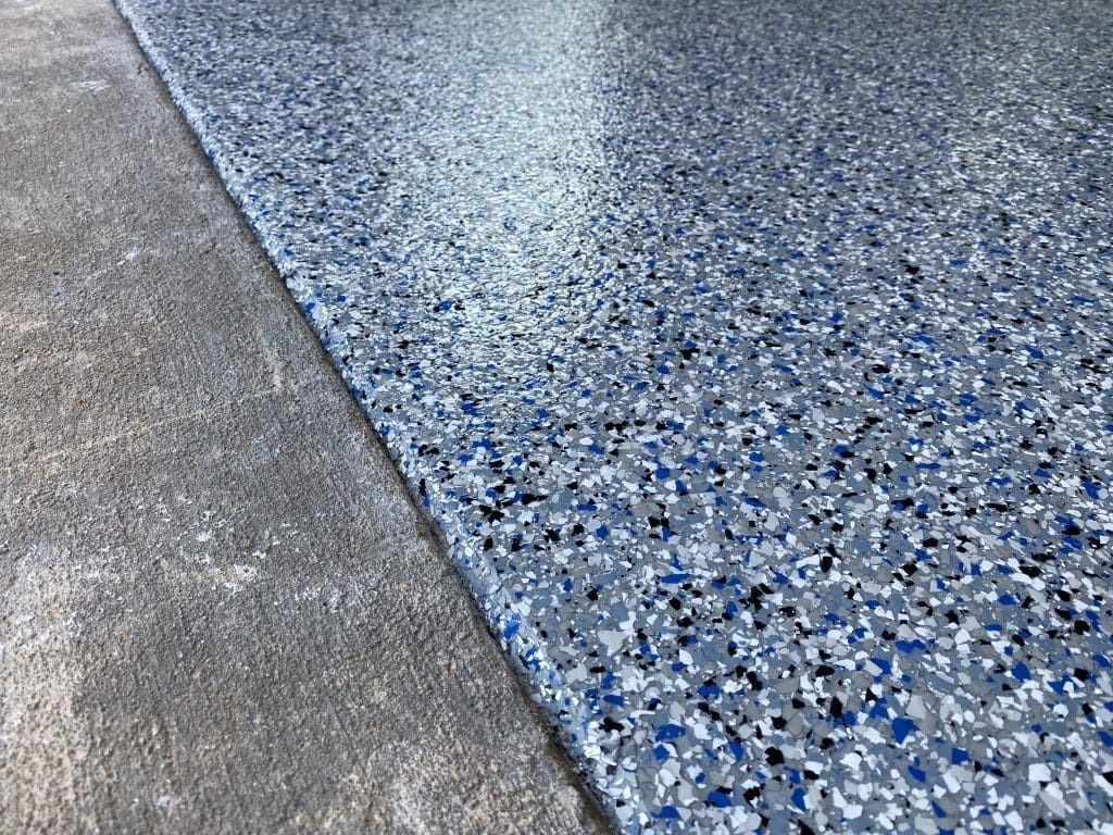 Concrete floor with blue, gray, and black fleck epoxy coating. The coating covers the right side.