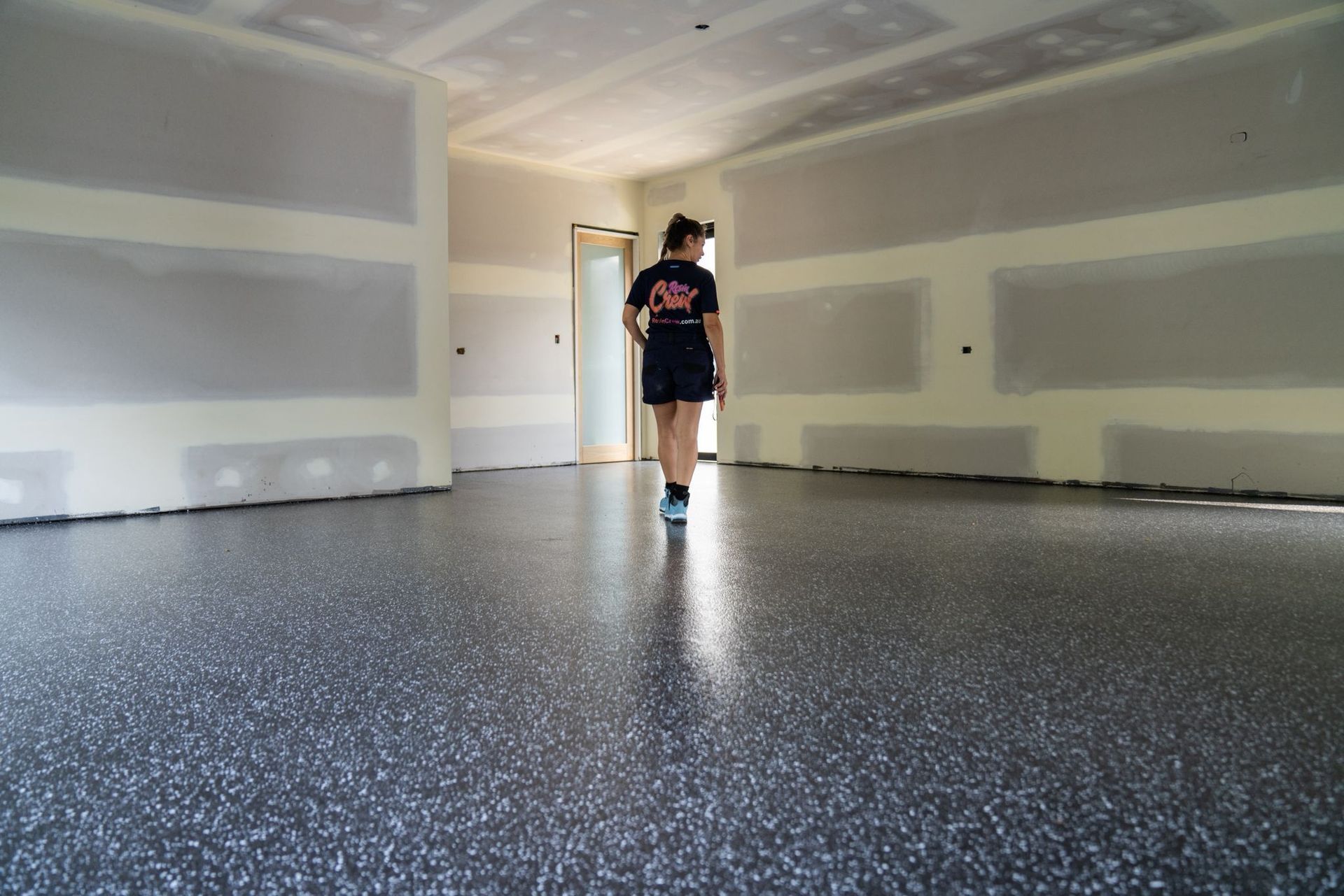 Person walking in a room with a shiny, speckled floor and drywall walls.
