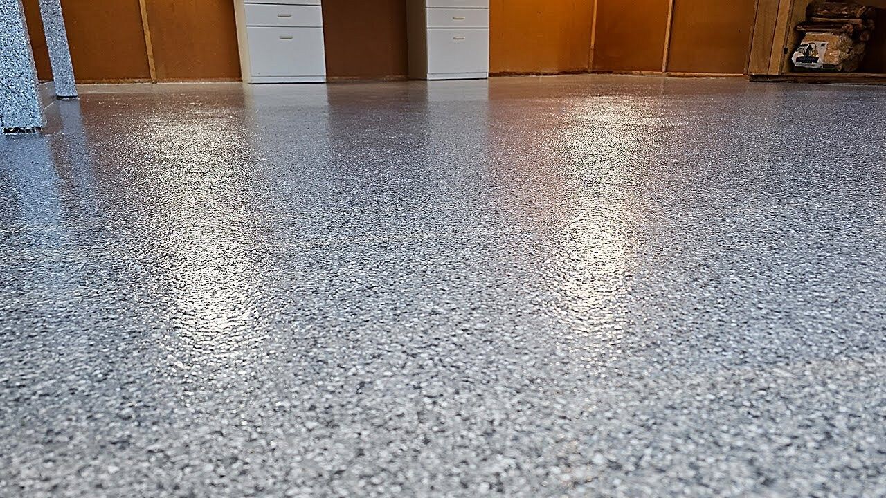 Gray speckled epoxy floor reflecting light. Brown and white backdrop.