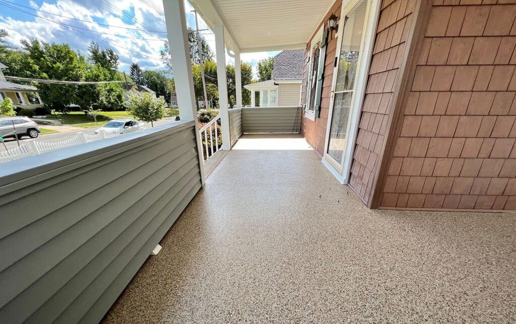 Porch with gray siding, brown speckle floor, white railing. Sunlight and neighborhood in background.