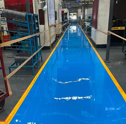 Blue epoxy floor in a factory with yellow safety lines, metal racks, and machinery.