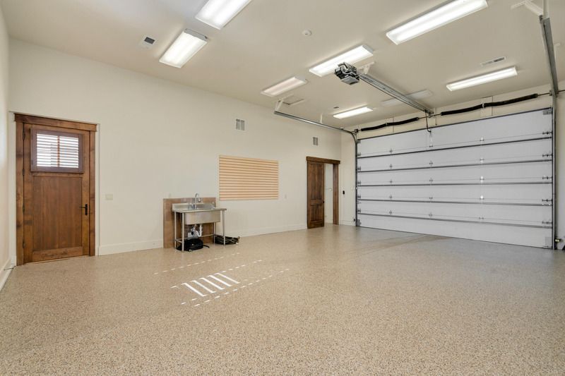 Spacious, empty garage with epoxy floor, overhead door, and two doors. Features a stainless steel sink.