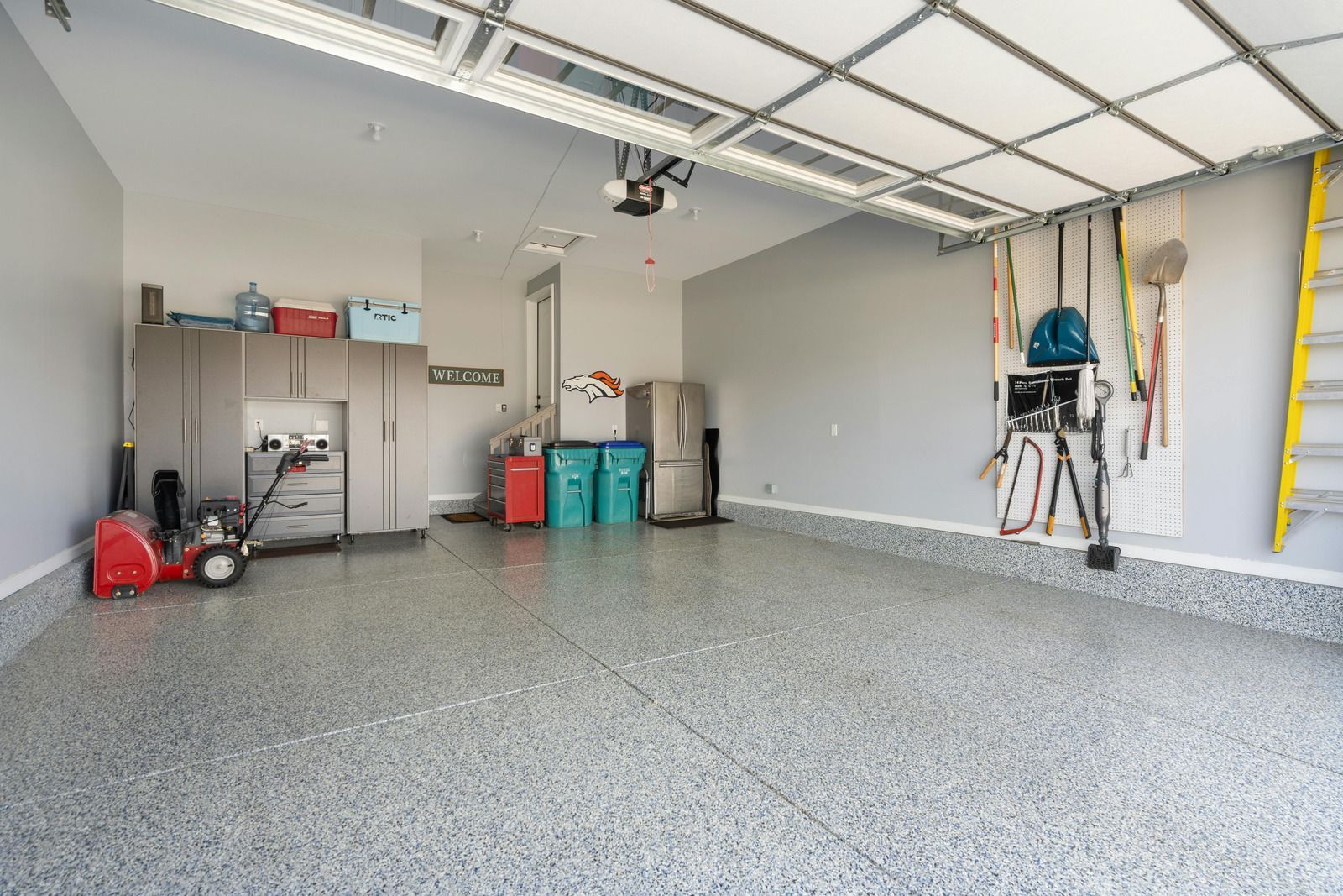 Empty garage with gray walls, speckled floor, storage cabinets, and tools.