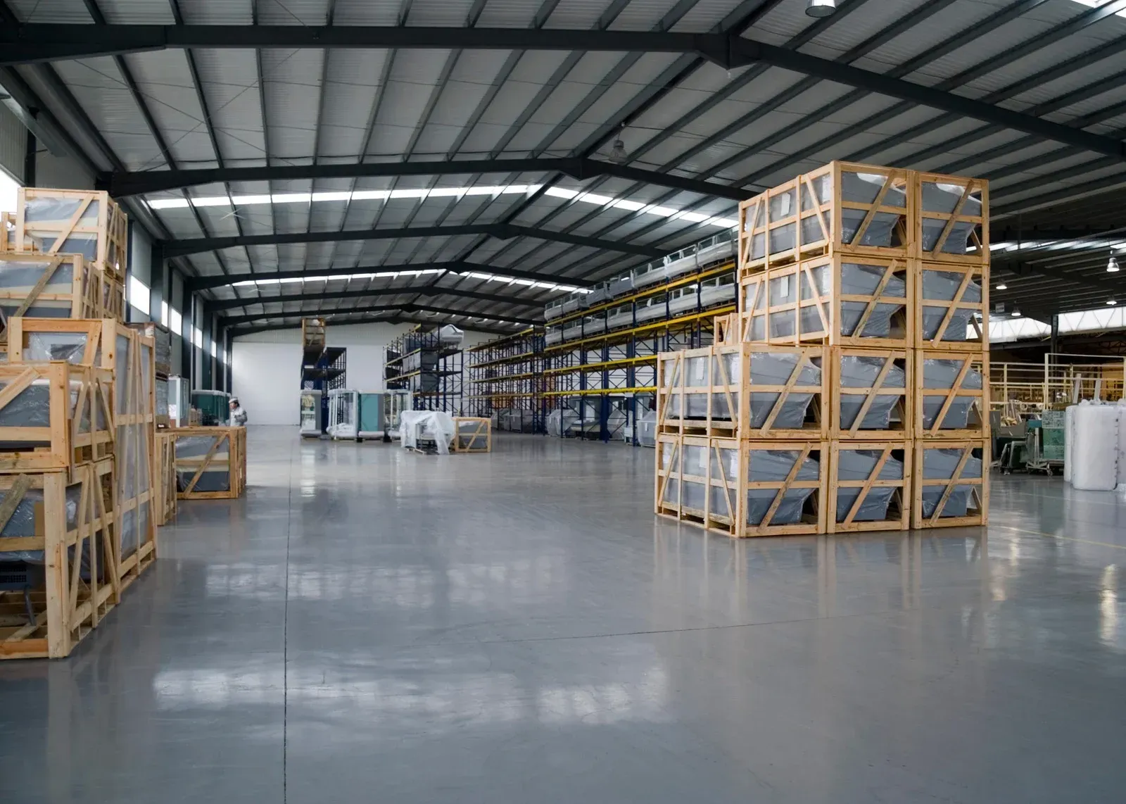 Warehouse interior with stacks of wooden crates, likely containing glass products.