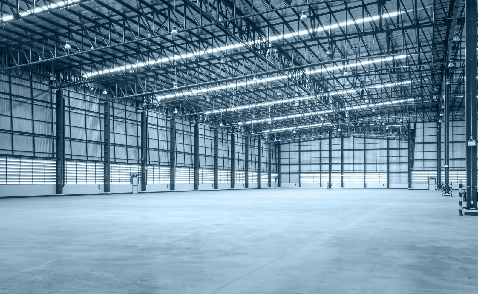 Empty warehouse interior with high ceiling, metal beams, and concrete floor.