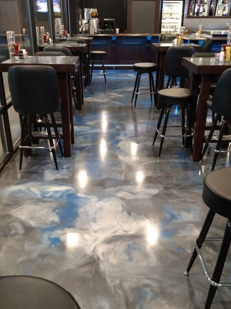 A restaurant interior with shiny, marbled floor; bar stools and tables; dark wooden bar and shelves in the background.