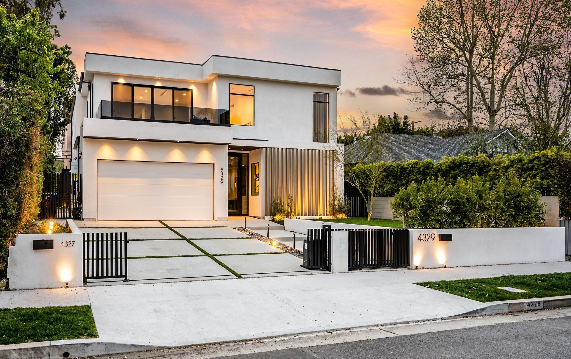 A large modern white house with a garage and a fence in front of it.