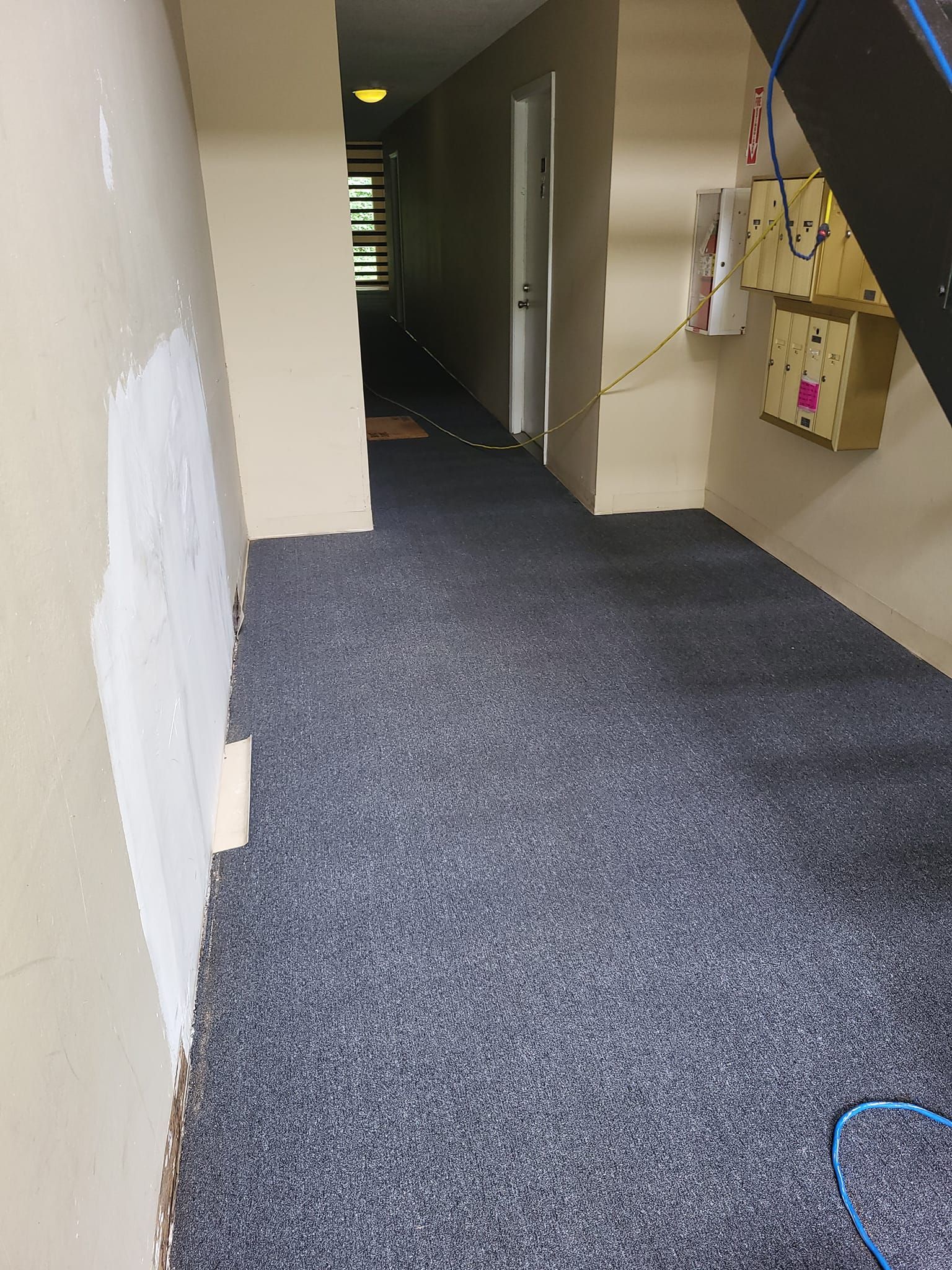 A long hallway with a gray carpet and a white wall.
