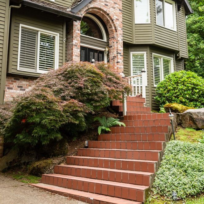 Brick steps lead up to a two-story green house, with a red brick archway and an overgrown bush.