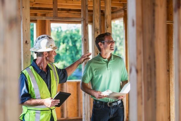 Construction worker points to the interior of a building under construction while talking to another man.