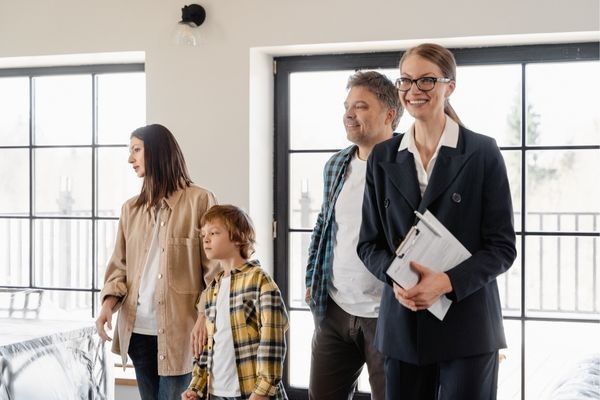 Real estate agent shows a family around a bright, modern home; smiles, windows.