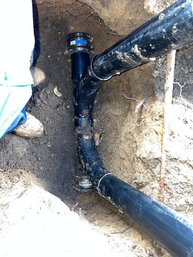 A gloved hand holds a dirty sink drain pipe, showcasing a severe blockage inside a kitchen cabinet.