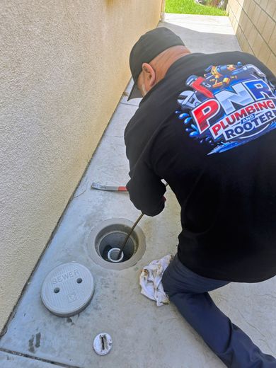 A person wearing gloves adjusts the blue handles of valves on gray industrial pipes mounted to a wall.