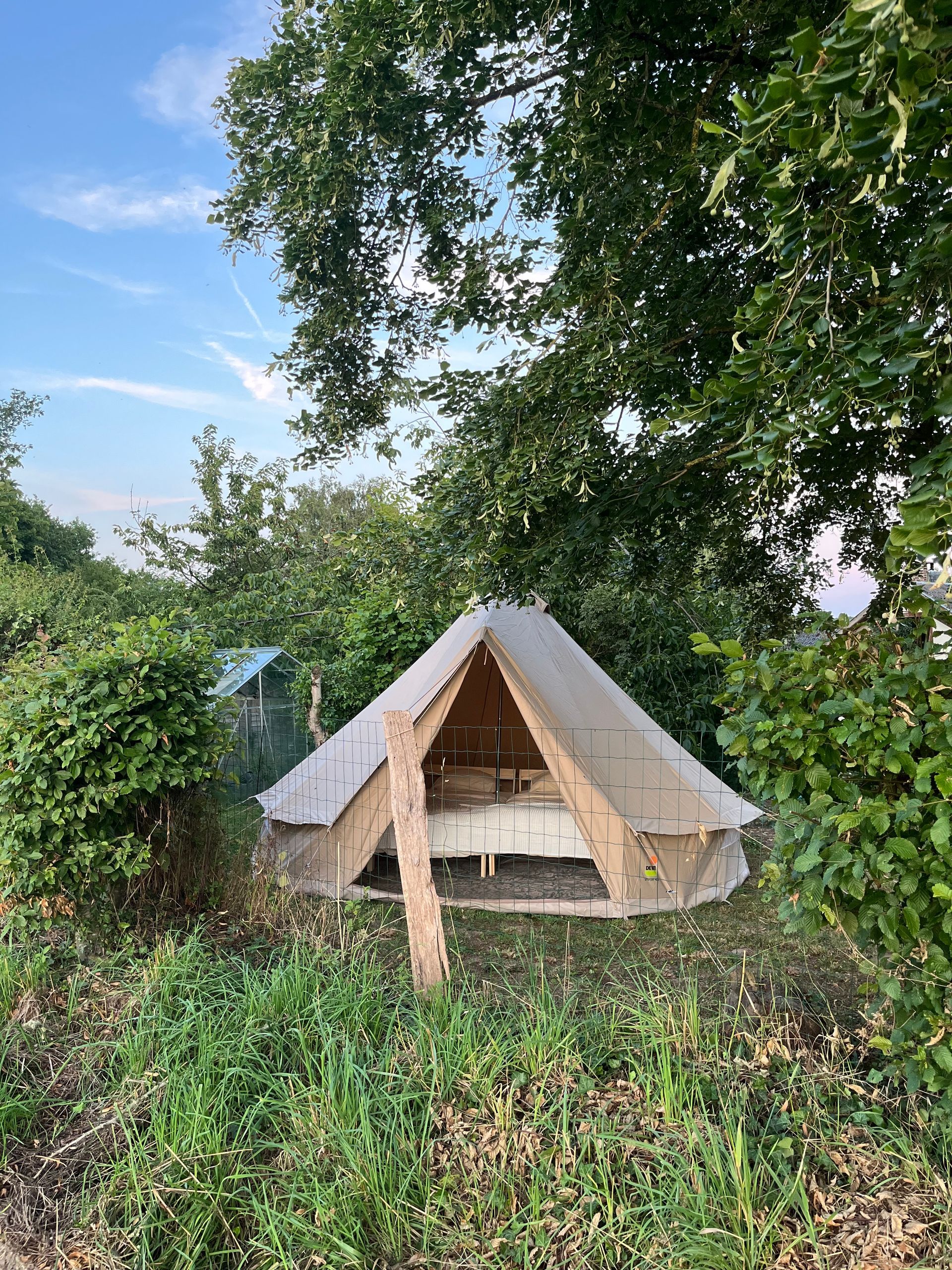 Canvas tent met houten frame, te midden van groen gebladerte, onder een blauwe hemel.