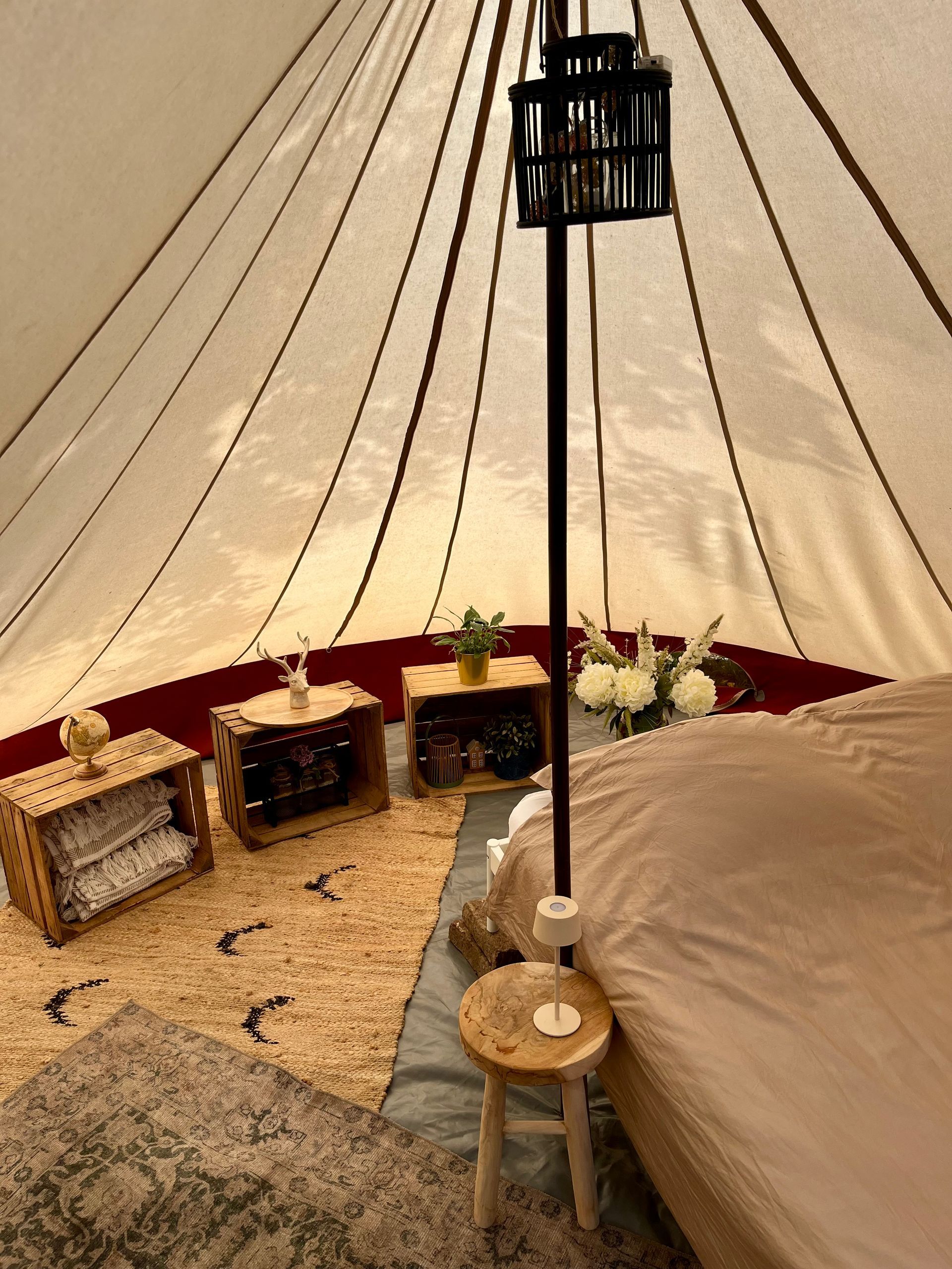 Gezellig tentinterieur met een bed, kleed en nachtkastjes. Aan een paal hangt een zwarte lantaarn.