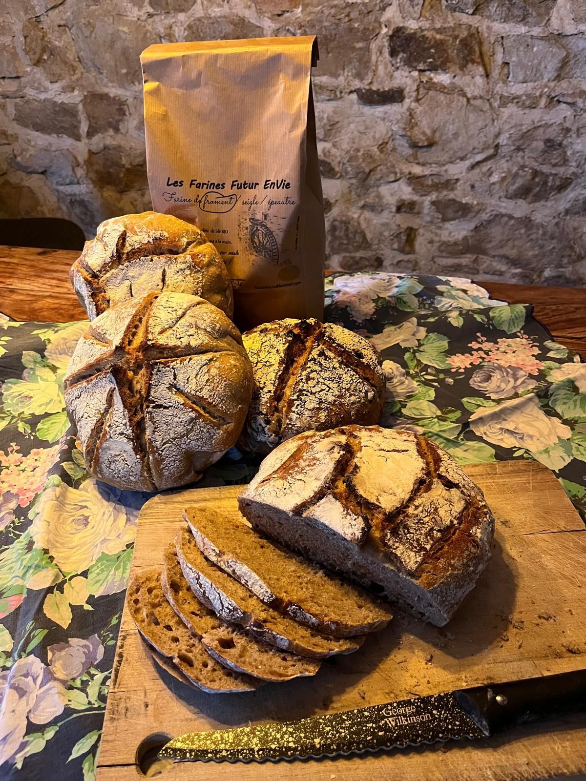 Broden van ambachtelijk brood met inkepingen, gesneden op een houten plank, naast een zak bloem.
