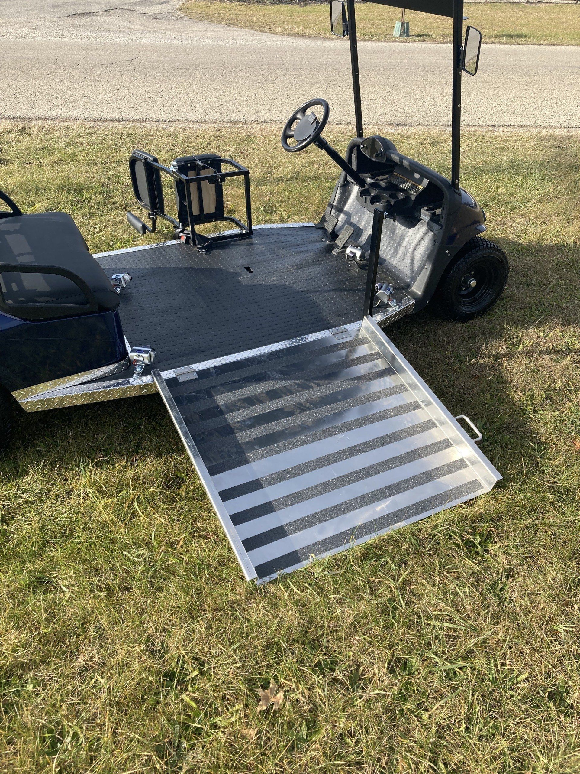 A golf cart with a ramp attached to it is parked in the grass.