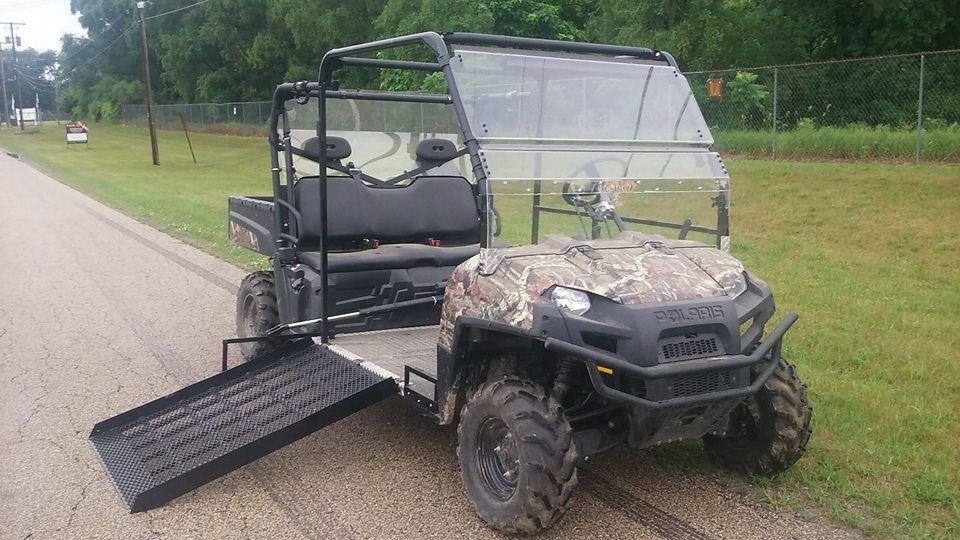 A polaris ranger with a ramp attached to it is parked on the side of the road.