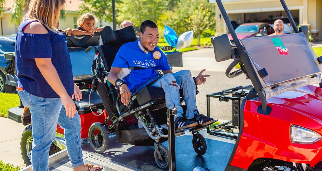 A man in a wheelchair is sitting next to a red golf cart.