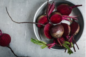 A bowl of beets with green leaves on a table.