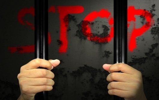 Hands on prison bars with word 'Stop'